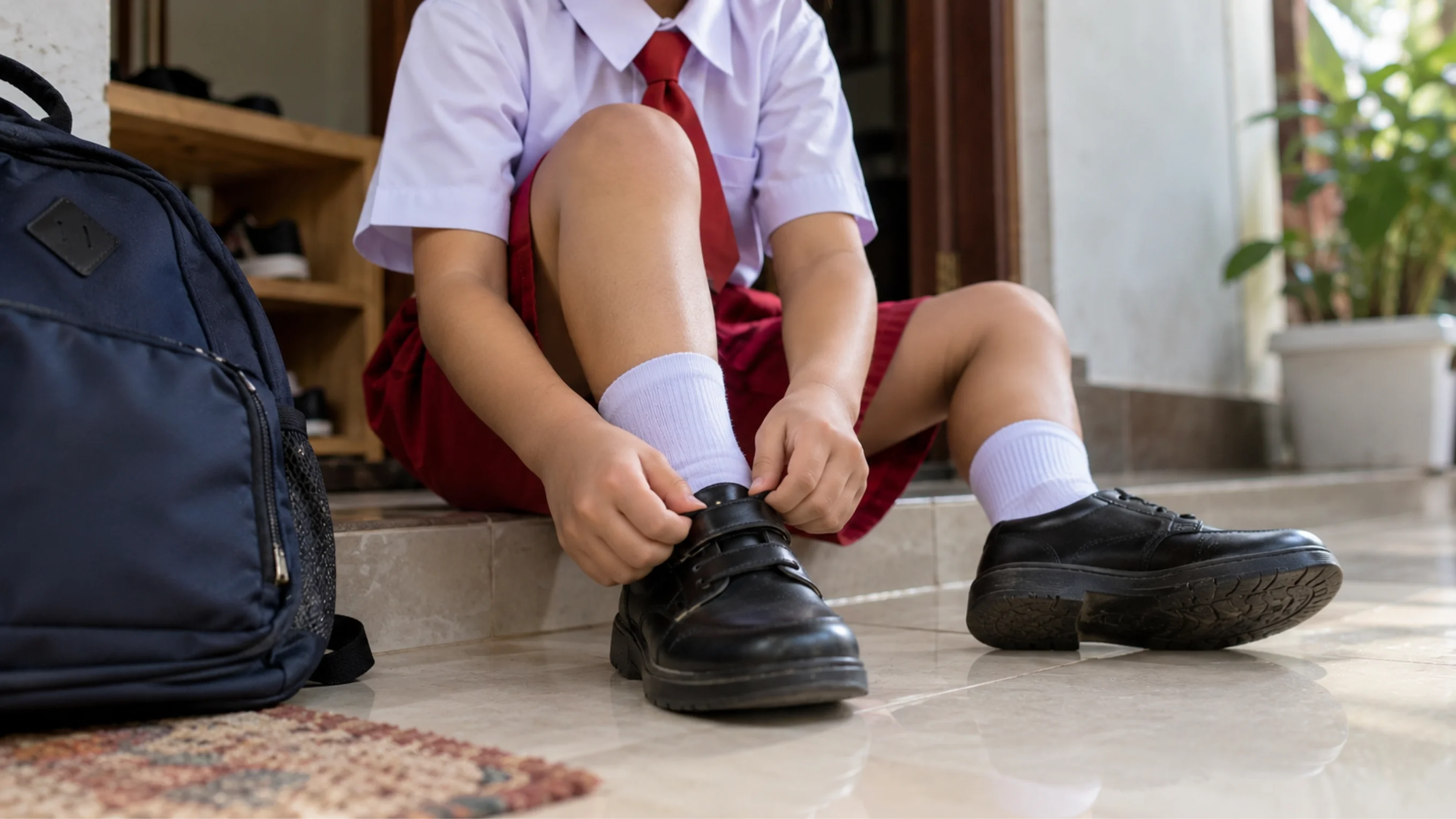 Anak usia 6 tahun berseragam SD memakai sepatu sendiri sebelum hari pertama sekolah, ilustrasi kesiapan masuk SD tanpa harus bisa calistung